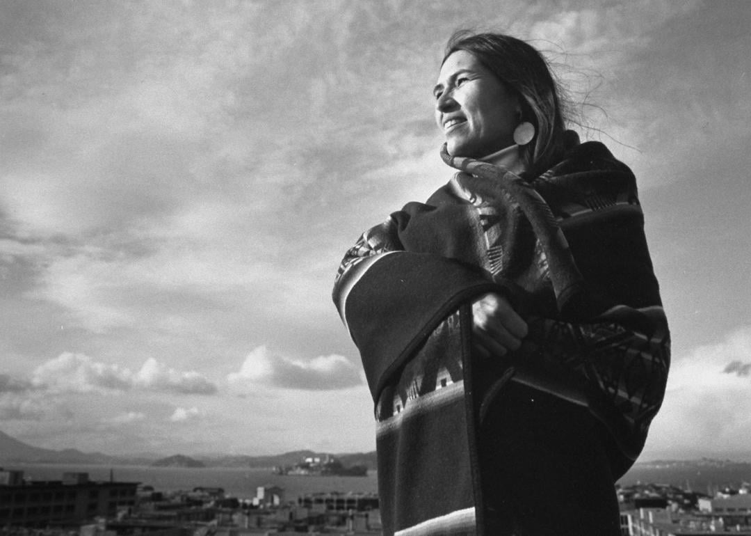 Indigenous activist Sacheen Littlefeather wrapped in a blanket posing on a rooftop in the Bay Area.