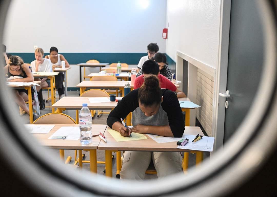 A group of students viewed through the window of their classroom door sitting at desks while taking exams.