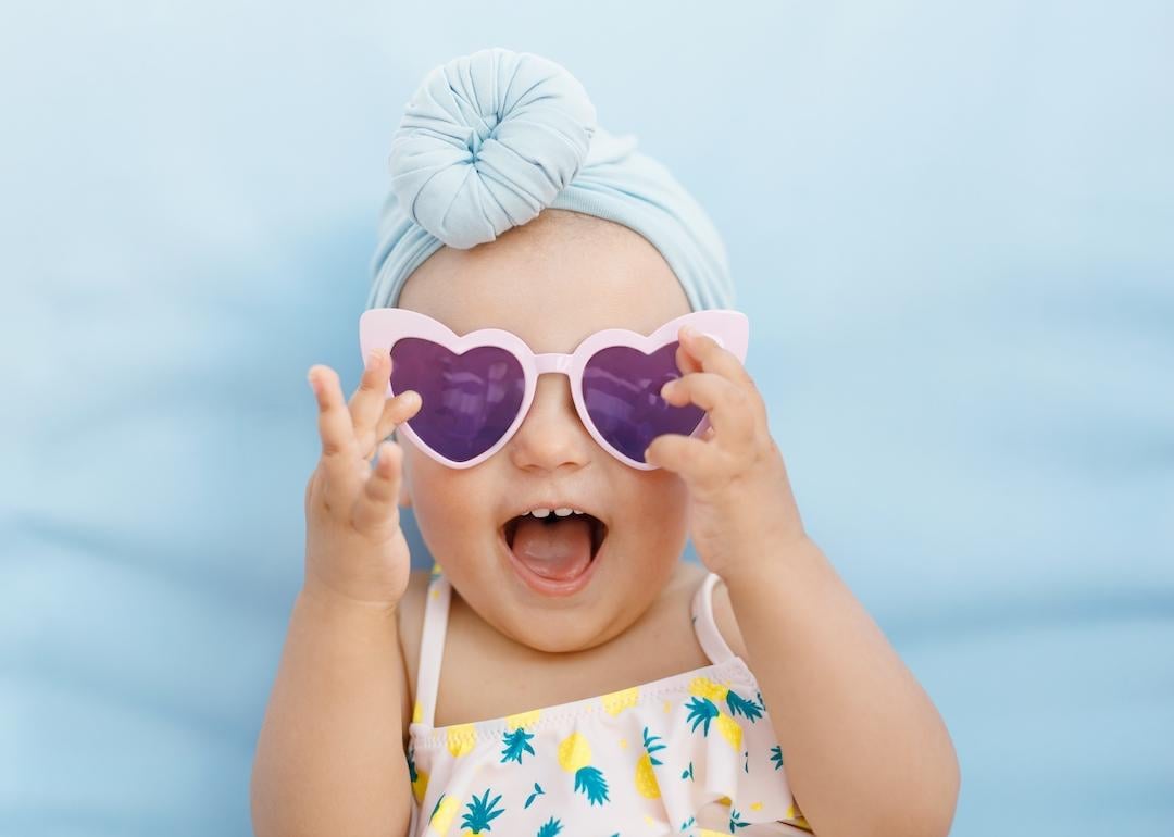 Baby wearing a turban and heart sunglasses on a blue background.