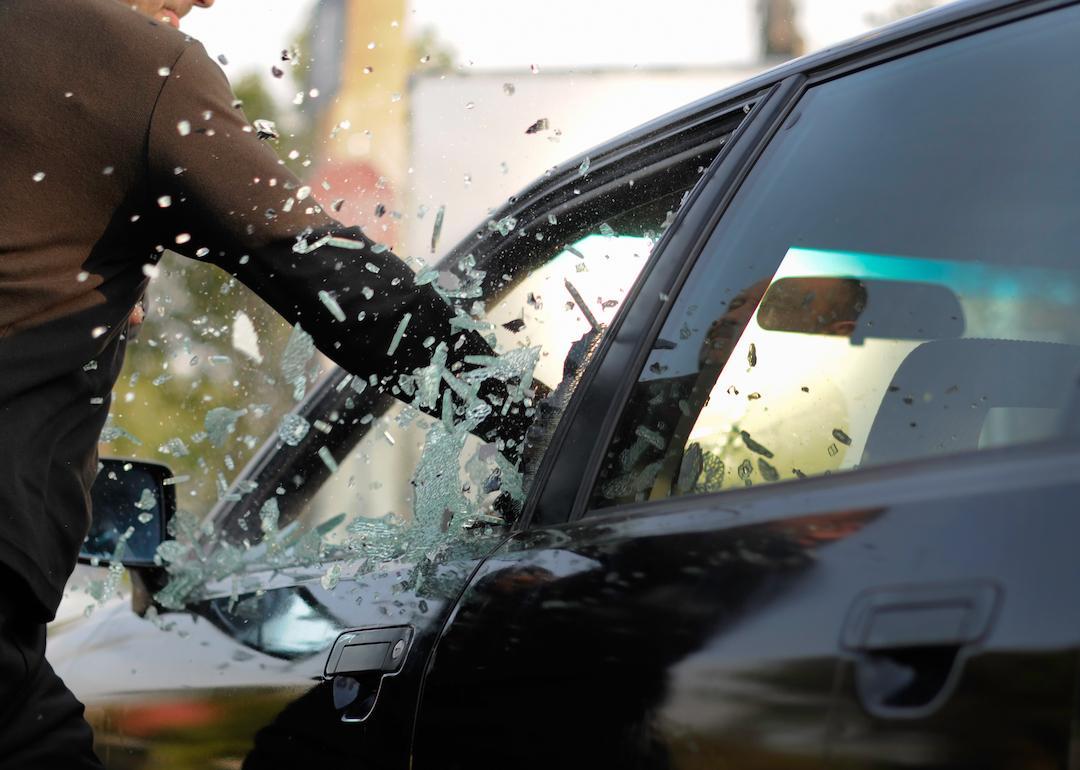 A car thief breaks a car window.