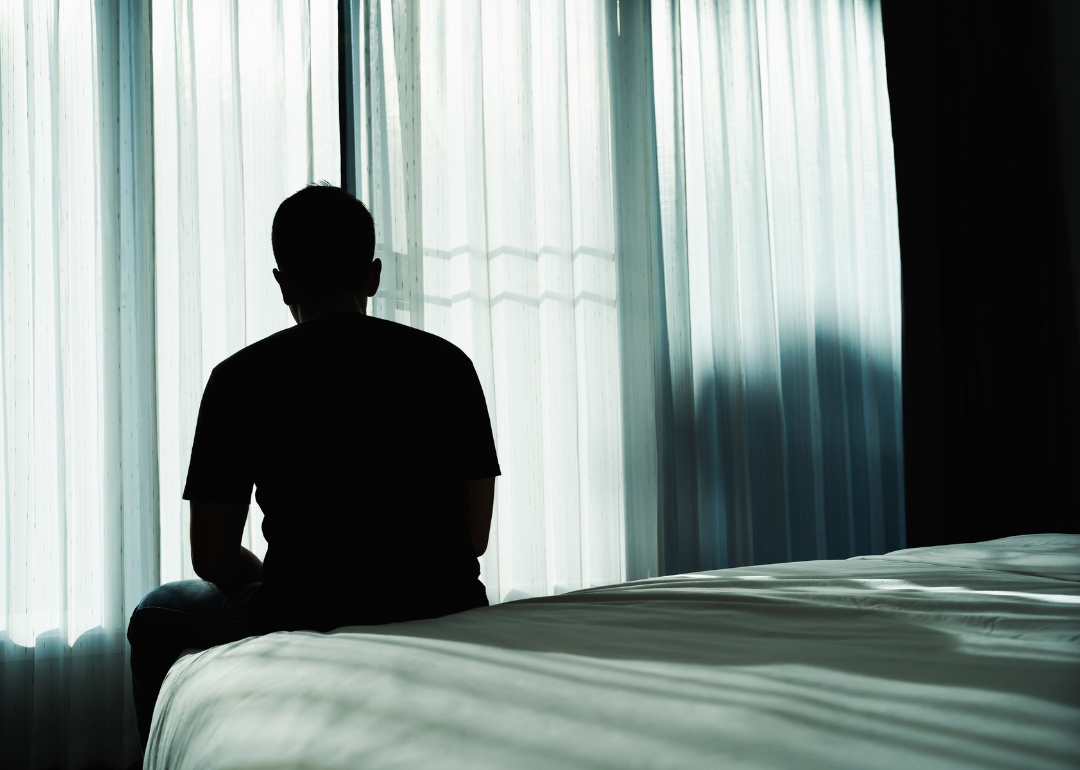 Silhouette of a man sitting in silence on the edge of the bed