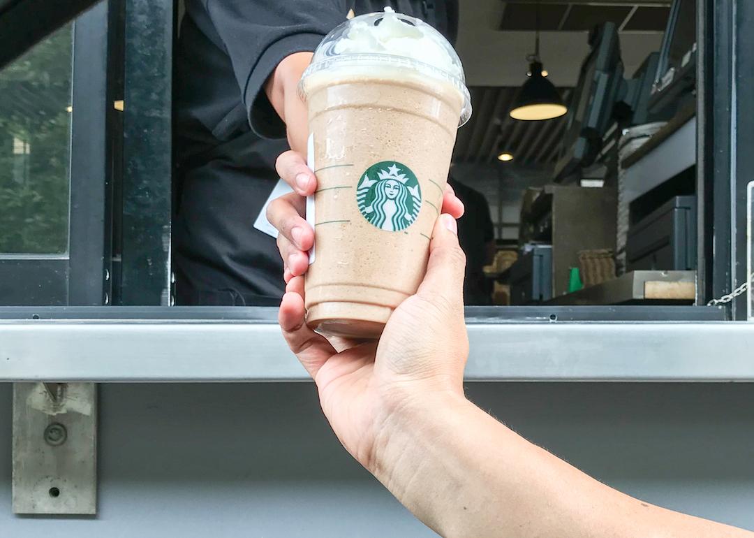 A Starbucks worker serves a venti frappuccino with whipped cream to a customer at drive-thru.