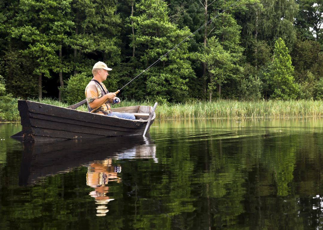 Fisherman sitting in the old, wooden rowboat and catching the fish on sunny day.