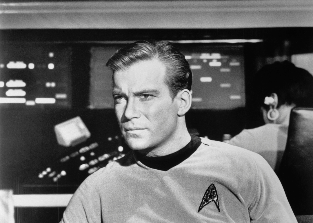 William Shatner as Captain James Kirk with a look of concern in close up of him seated in the Starship Enterprise in an episode of "Star Trek".