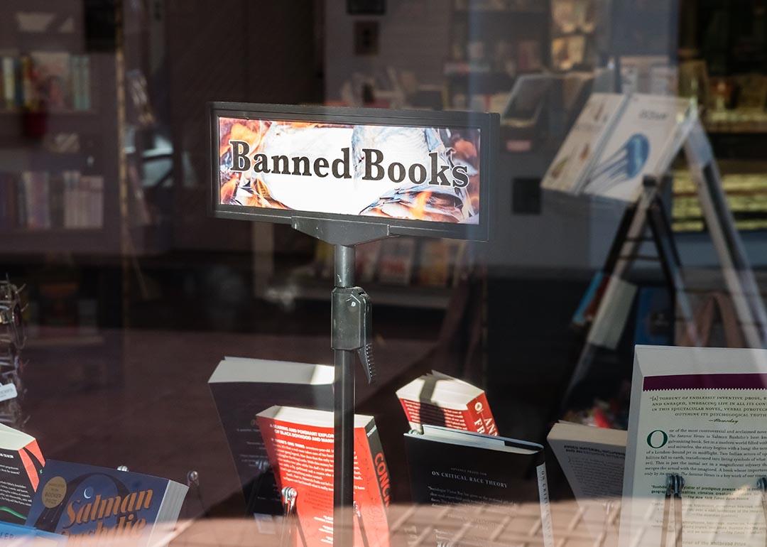 View of bookstore window where a "banned books" sign is displayed above books for sale.