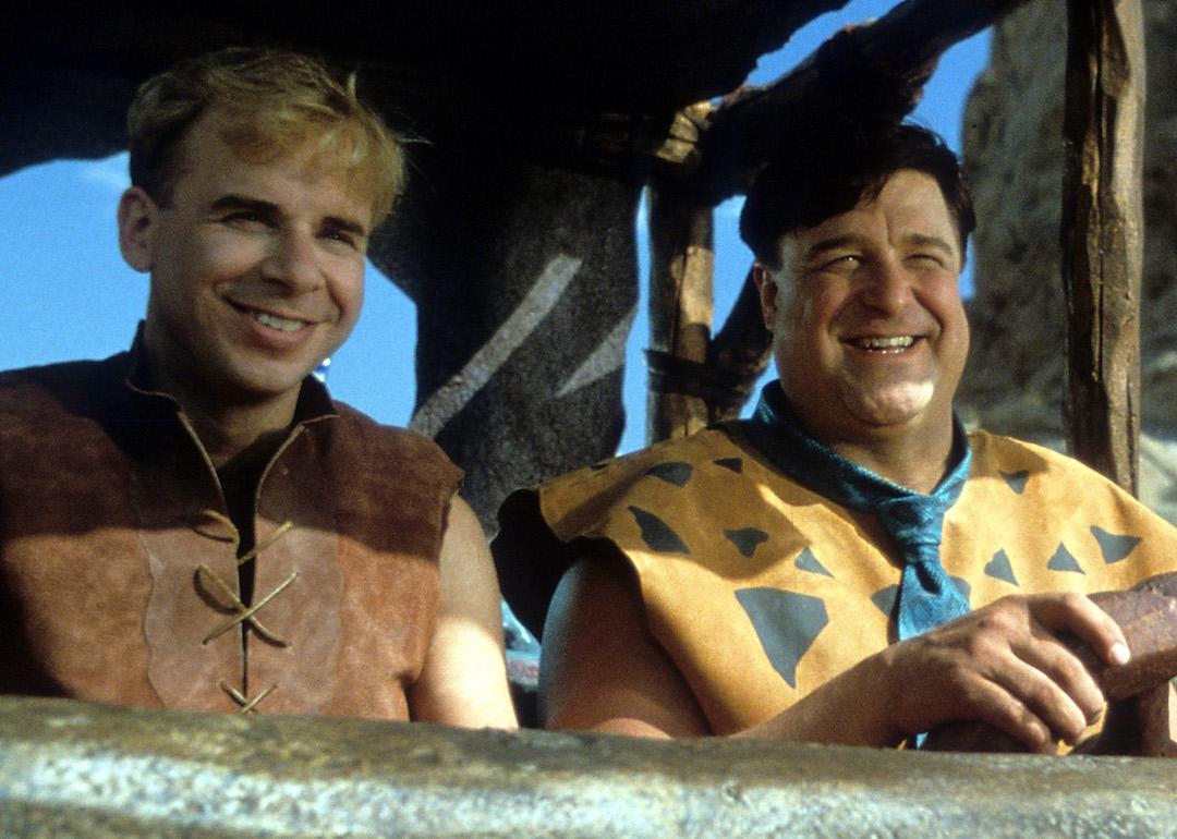 Actors Rick Moranis and John Goodman riding together in a scene from the 1994 film 'The Flintstones.'