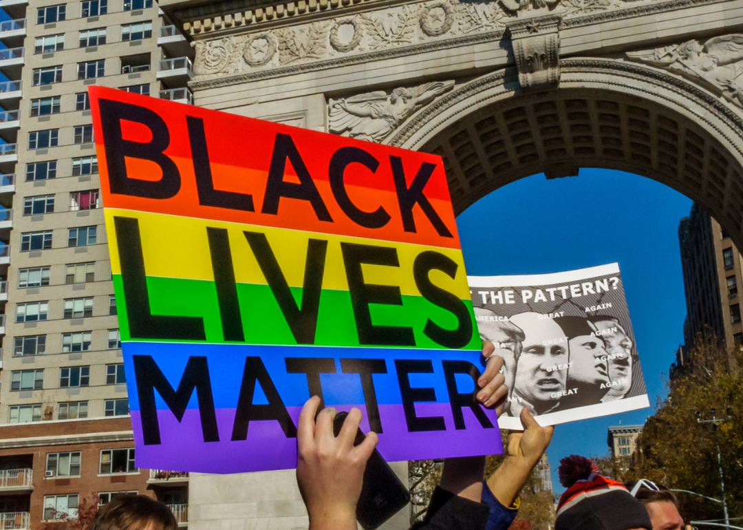 Student protesters from NYU holding up a sign that says "Black Live Matter" with a Pride flag in the background, in Washington Square Park, New York City
