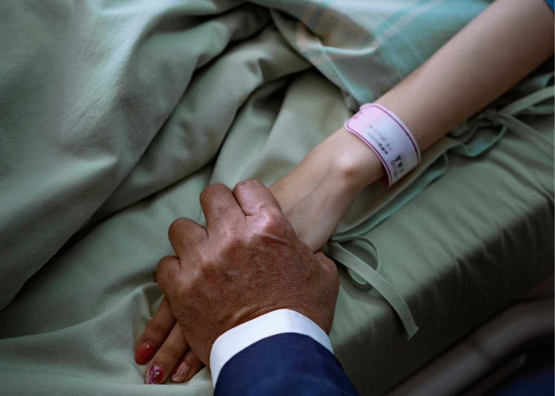 A loved one holds the hand of a patient in hospital bed