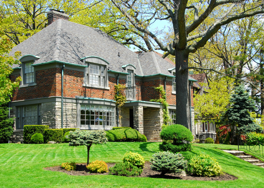 A large two-storey brick and stone house with a well-manicured front lawn in an affluent neighborhood