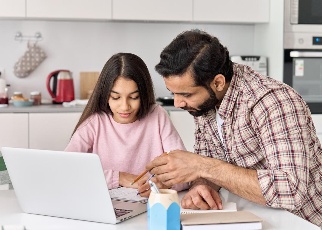 A father and his daughter using a laptop and writing down notes to help with homework.