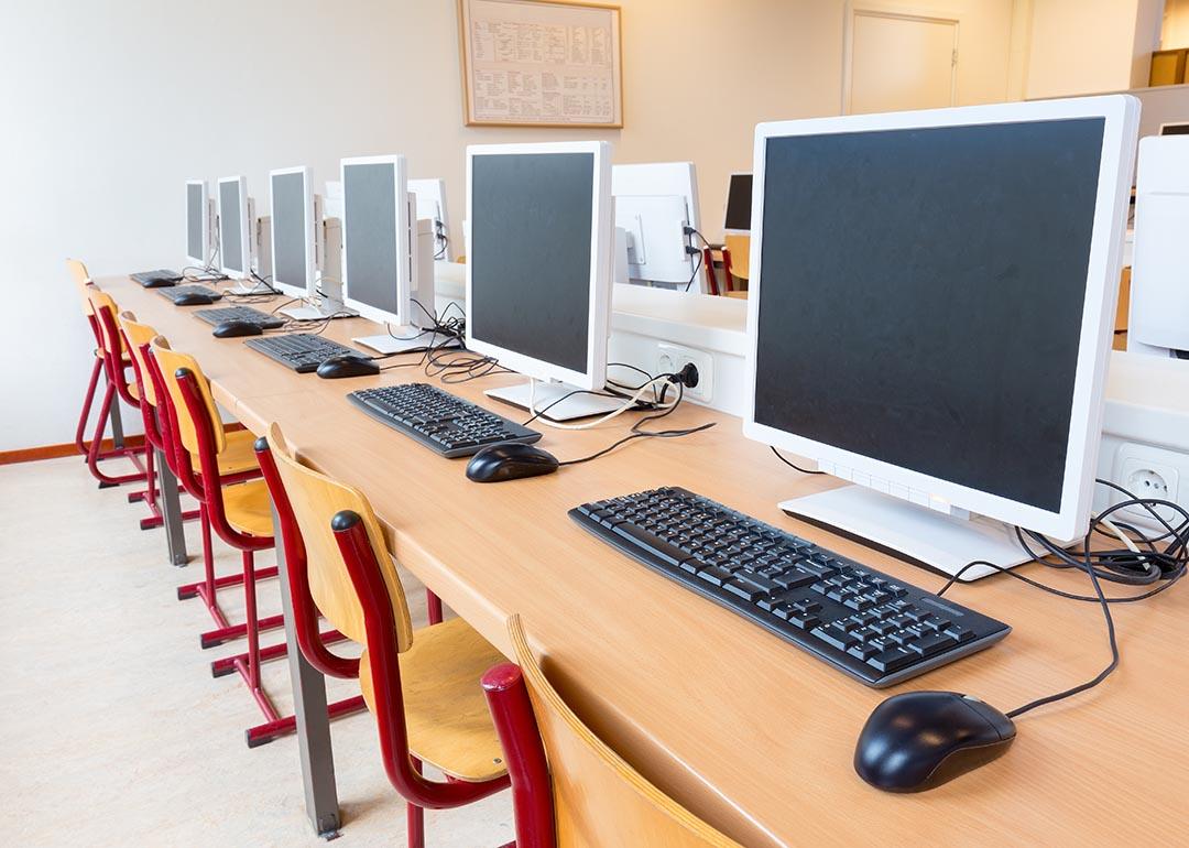 A row of computers and chairs in a school computer lab.