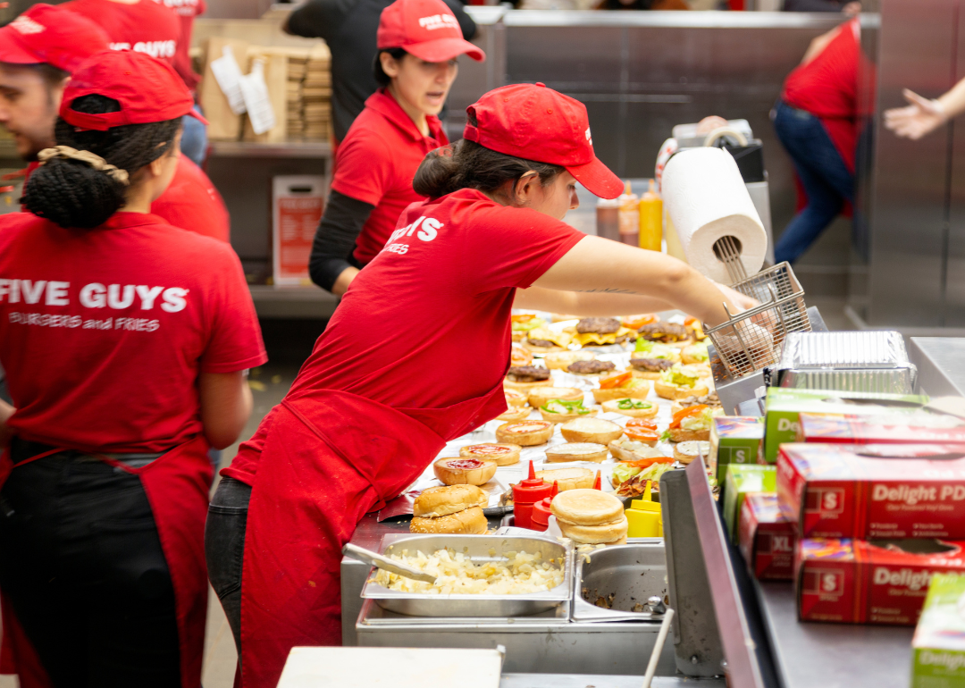 Servers assembling food in the kitchen of a Five Guys 