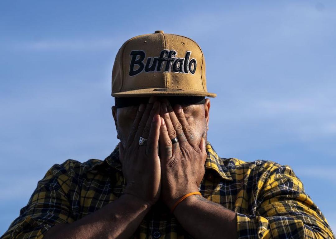A person in Buffalo covers their face with their hands near a memorial for the victims of a mass shooting at Tops Friendly Market in 2022 in Buffalo, New York.