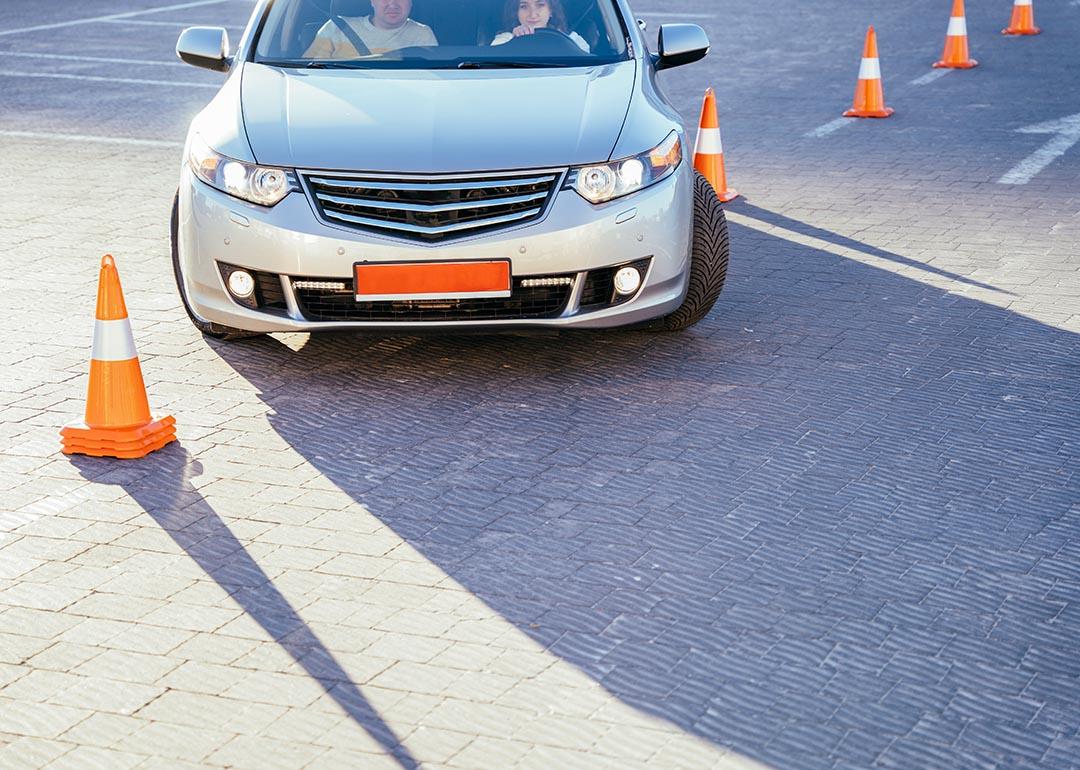 A young female student driver is being taught how to go around traffic cones.