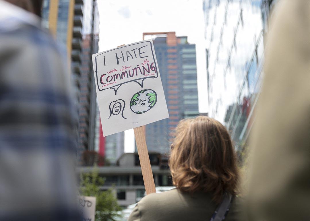 A demonstrator holds a sign that reads "I hate commuting" as Amazon employees and supporters gather during a protest against recent layoffs, a return-to-office mandate, and the company's environmental impact.