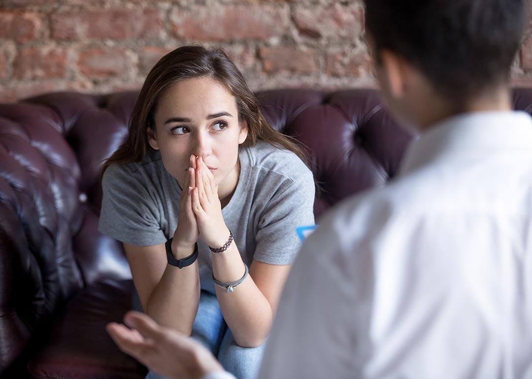 A young woman seemingly in a therapy session sitting on a couch with a thinking gesture.