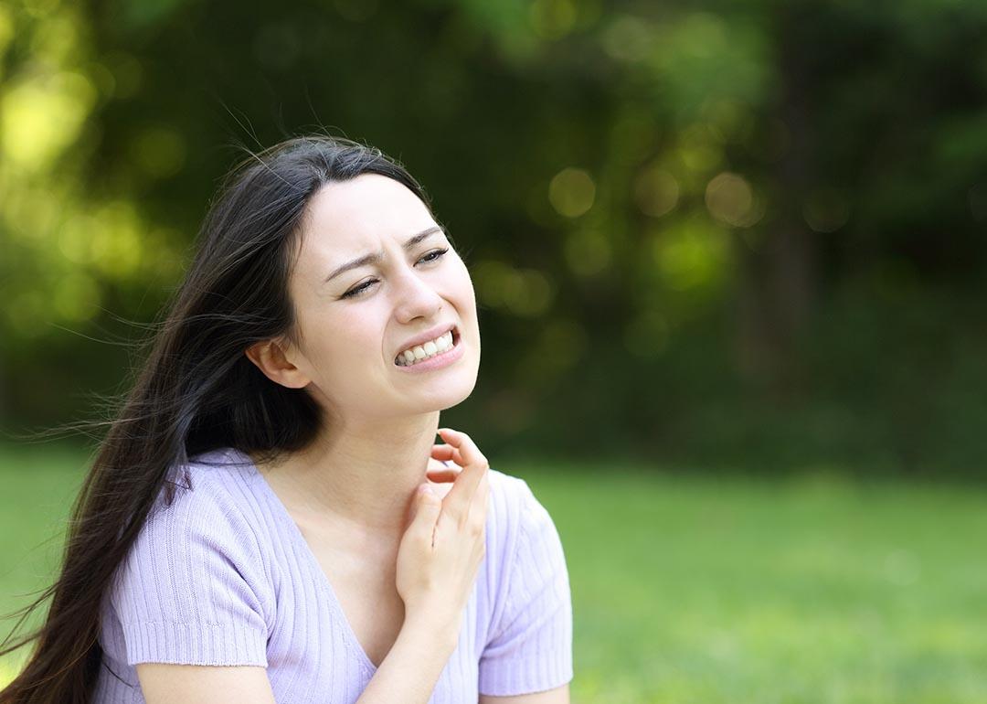 A woman scratching her neck while seated outdoors.