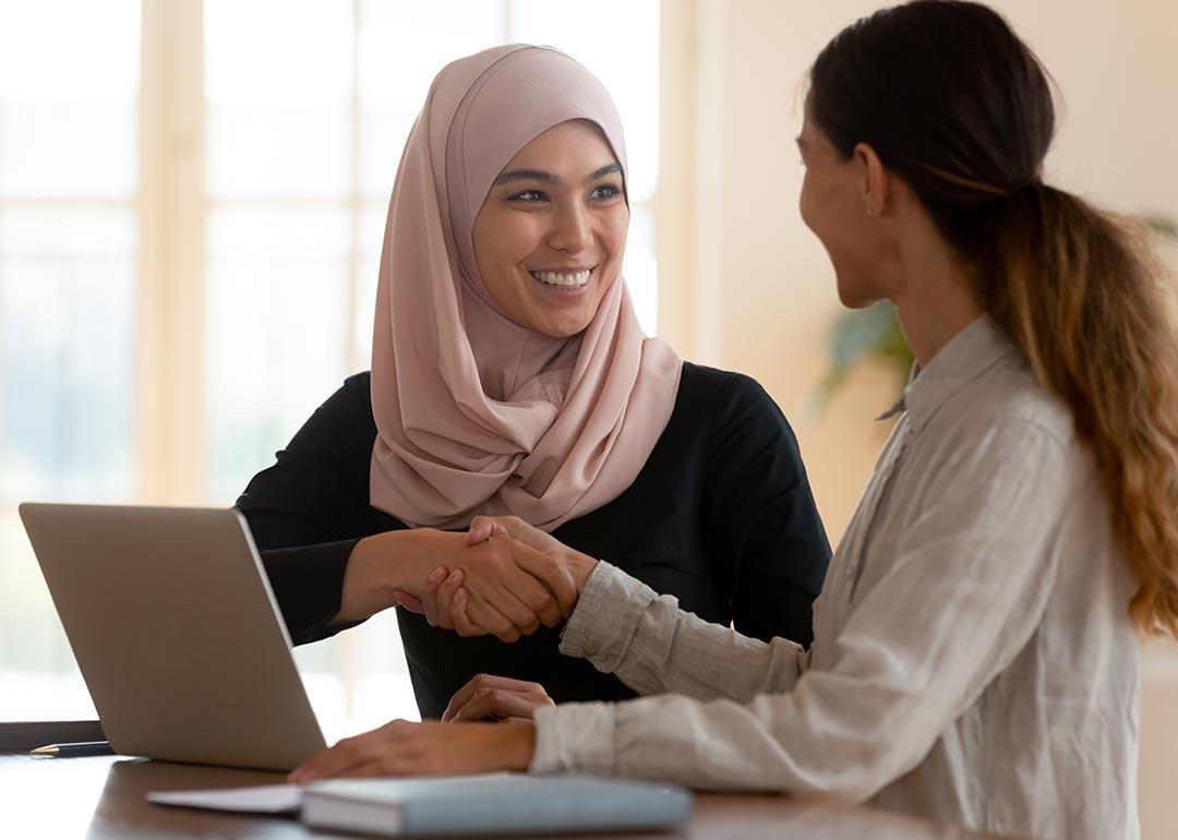 A muslim woman shaking hands with a female professional seemingly in agreement during a discussion.