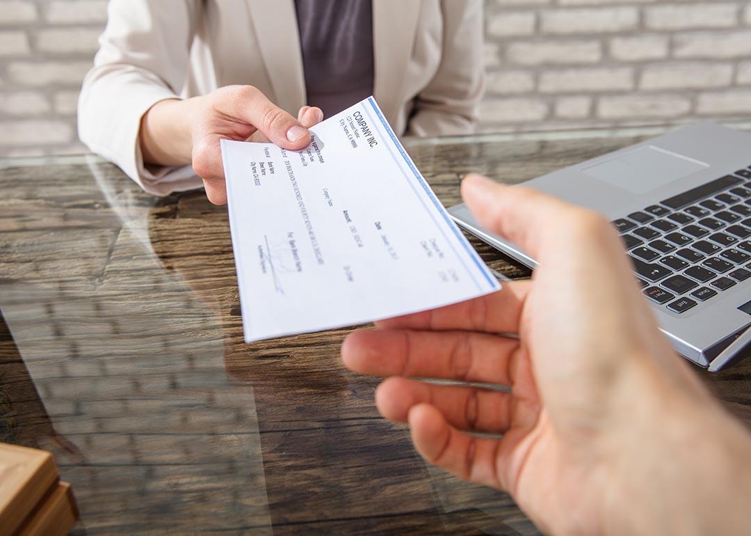 Hand receiving check from business person across table.