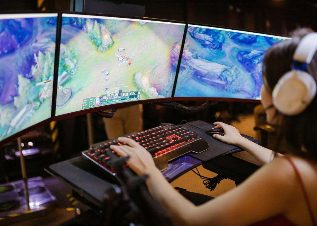 A female gamer is focused playing a PC game displayed on three monitors.