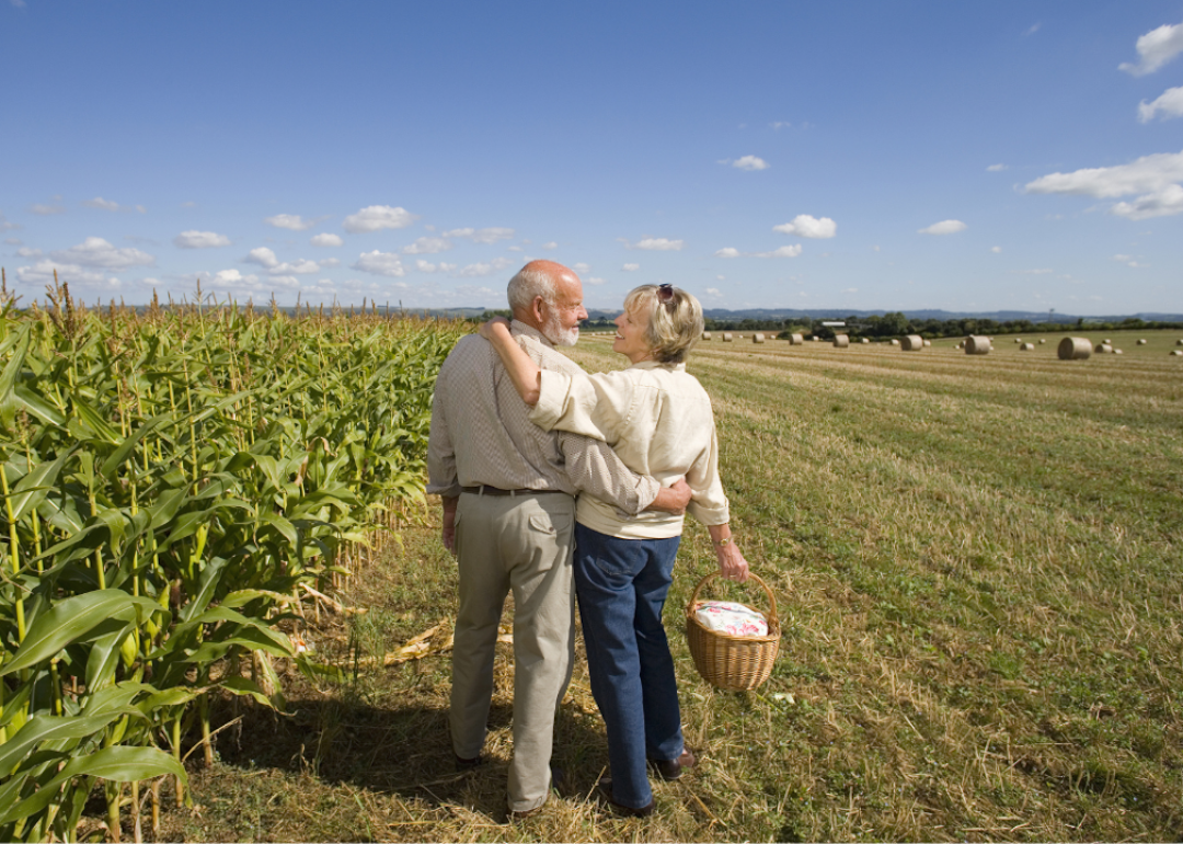 Senior couple standing next to a cornfield embracing and smiling at each other.