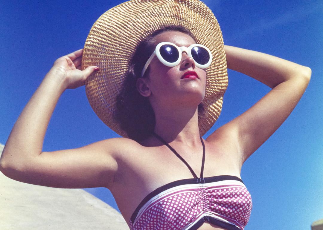 Person wearing sunglasses and a wide-brimmed hat sunbathing in 1944.