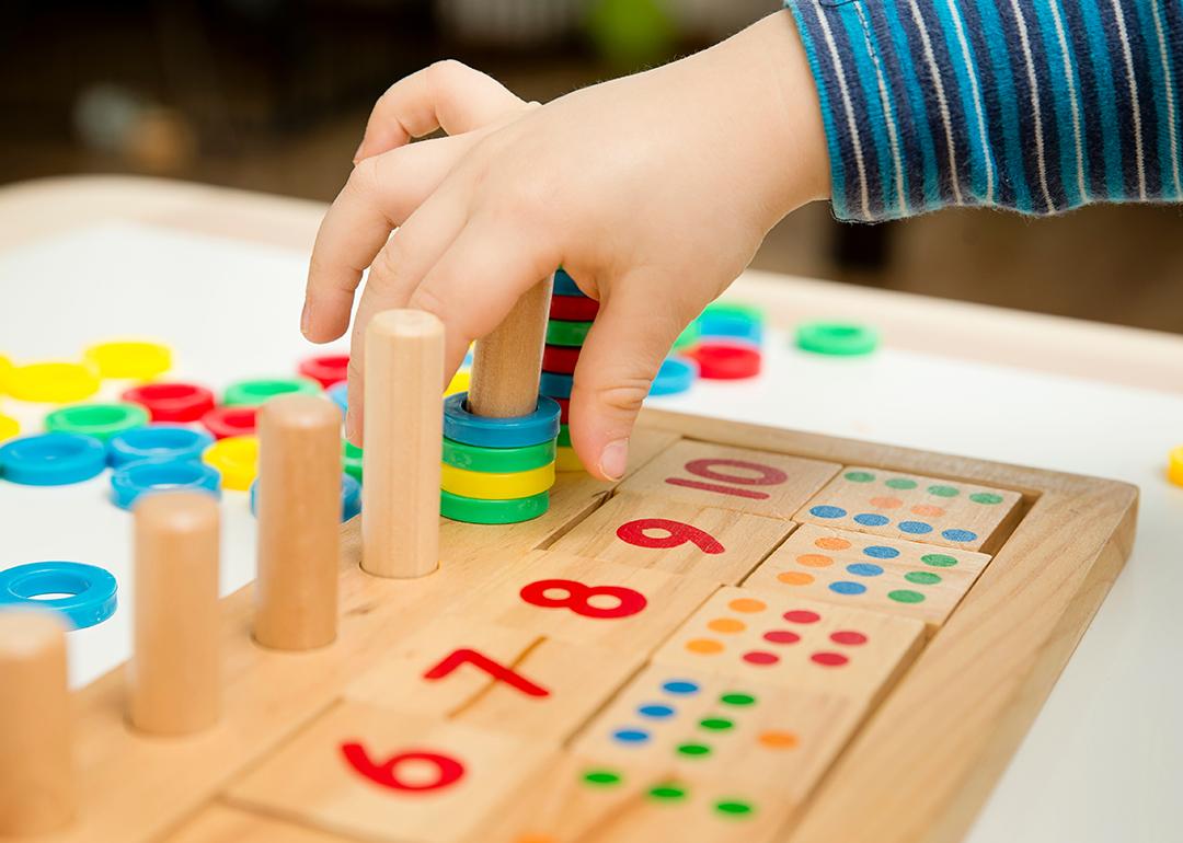 Child playing with different color wooden rings on a board with painted numbers and dots.