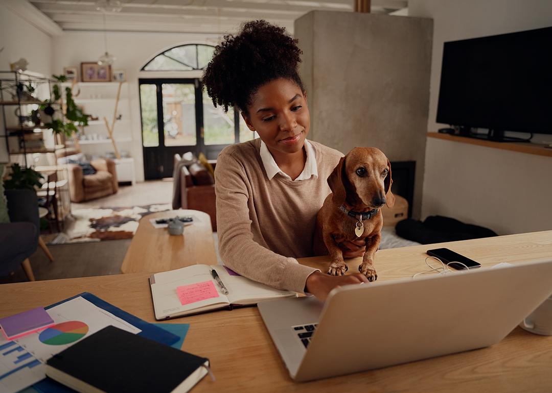 A woman working from home is sitting happily with her dog using a laptop.
