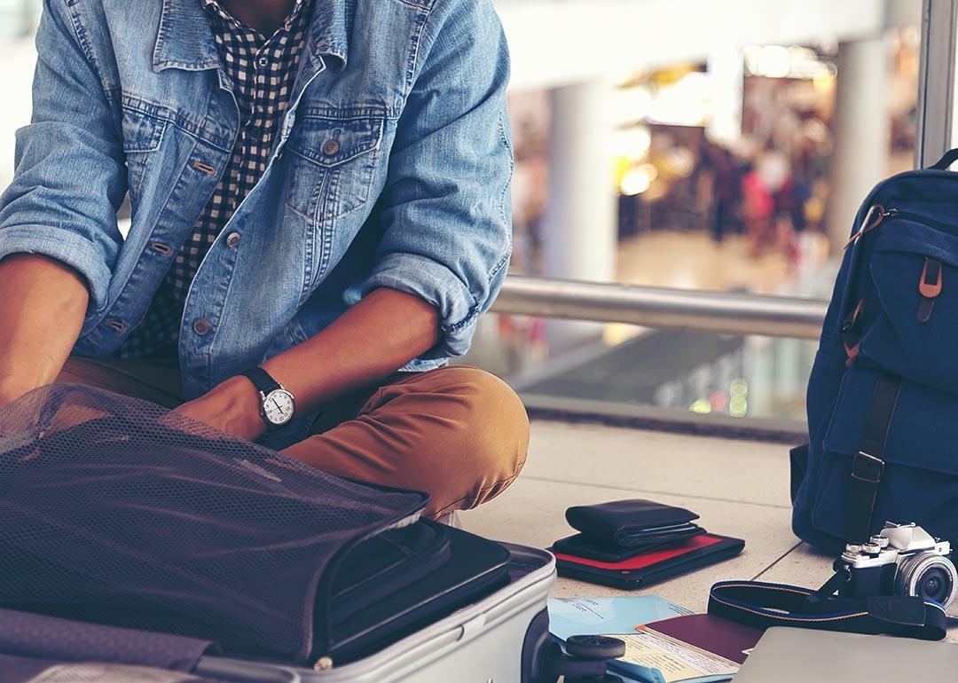 A male traveler is sitting on the ground of an airport while fixing items from his travel bags.