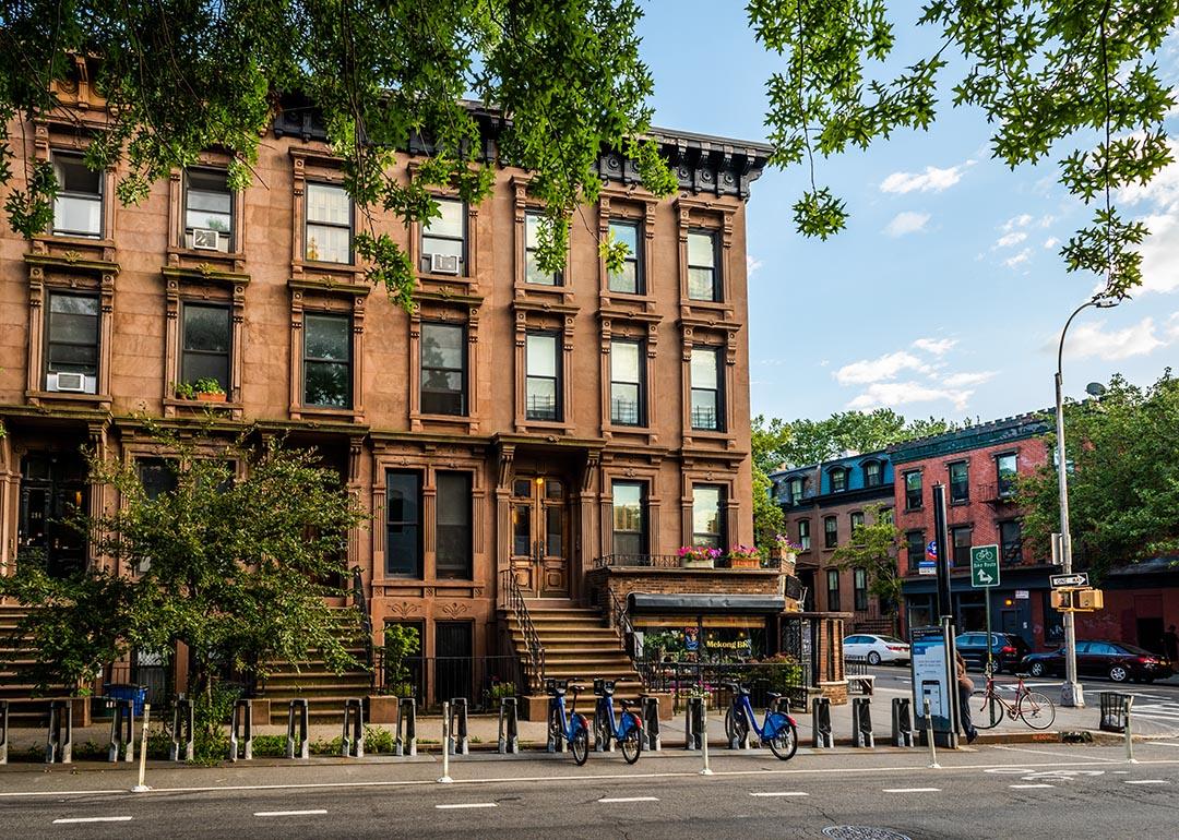 Scenic view of a classic Brooklyn brownstone block with a long facade and ornate stoop balustrades on a summer day in Clinton Hills, Brooklyn.