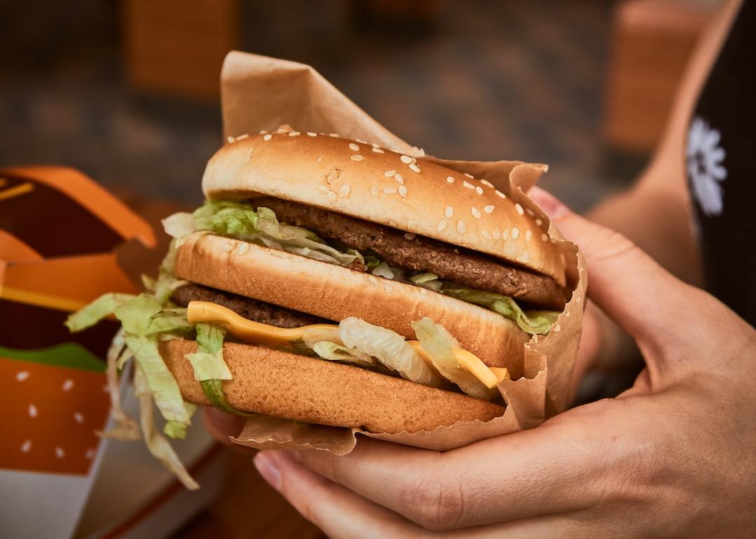 Double cheeseburger in customer's hands at fast-food restaurant.