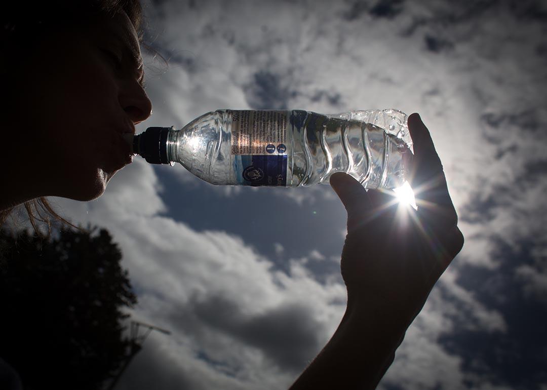 Silhouette of person drinking bottled water backlit by sun.