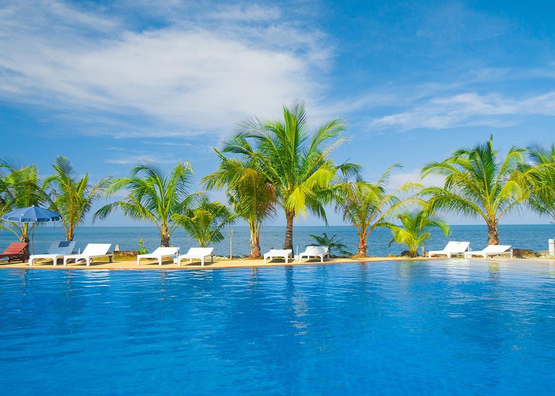 View of pool with palm trees and blue sky and ocean in background.