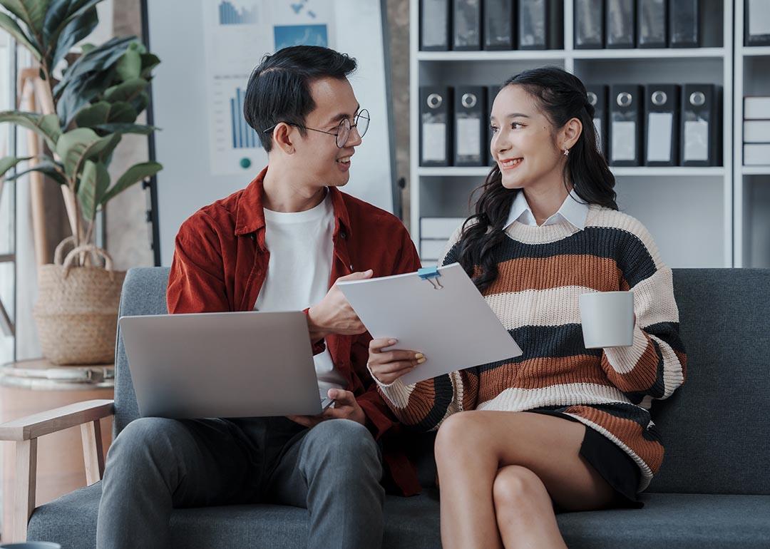 A couple sitting on a sofa where the woman is holding a set of forms and both are engaged in discussion.