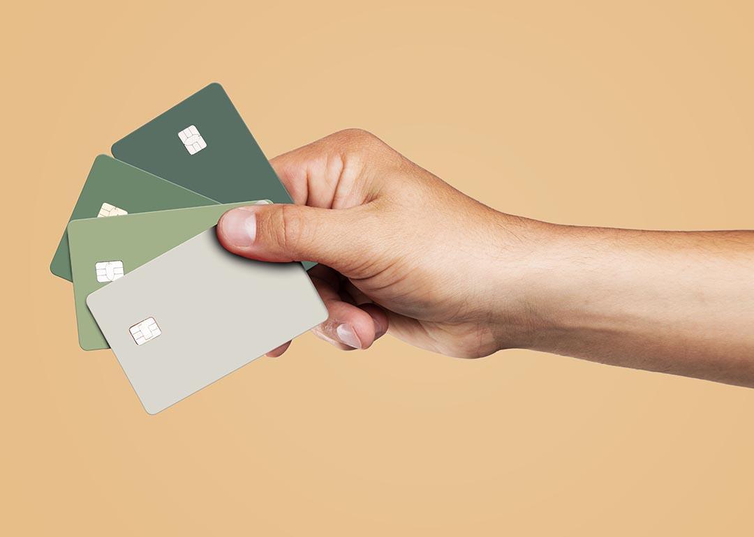 A person's hand is holding four credit cards displayed over a beige background.