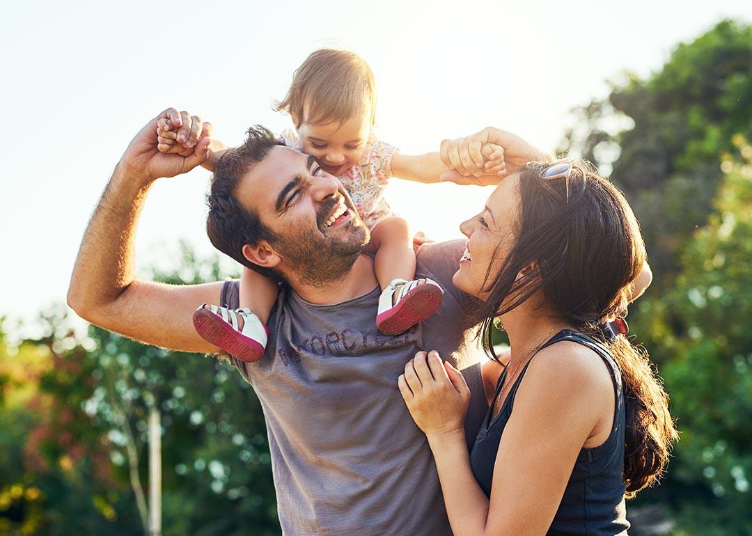 A small child sits on a man's shoulders while a woman makes faces and laughs along.