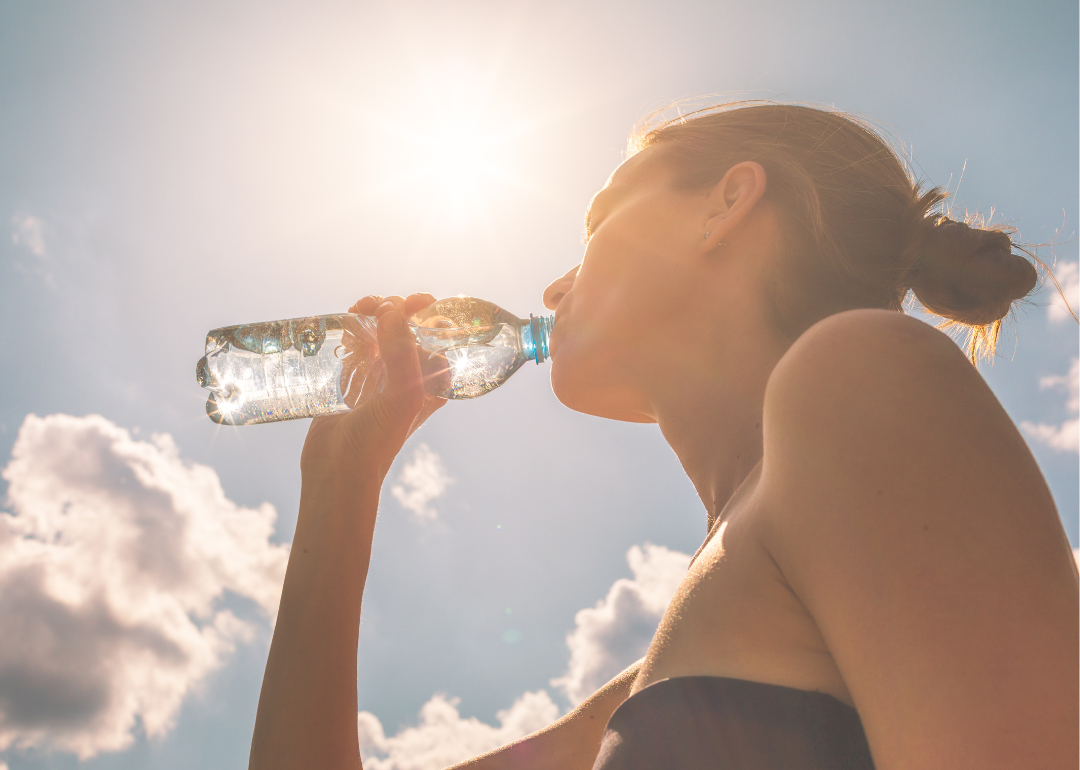 Woman drinking water out of a plastic bottle on a hot sunny day
