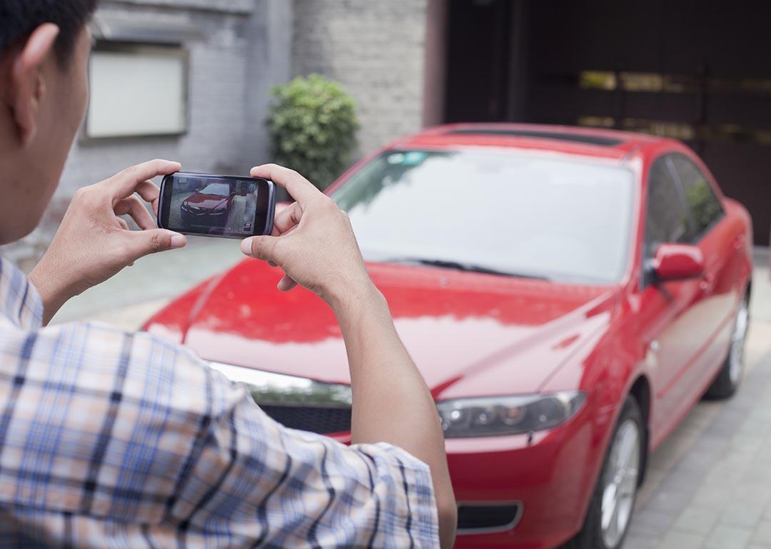 Young person in foreground taking photo of a red car from the front with a smartphone..