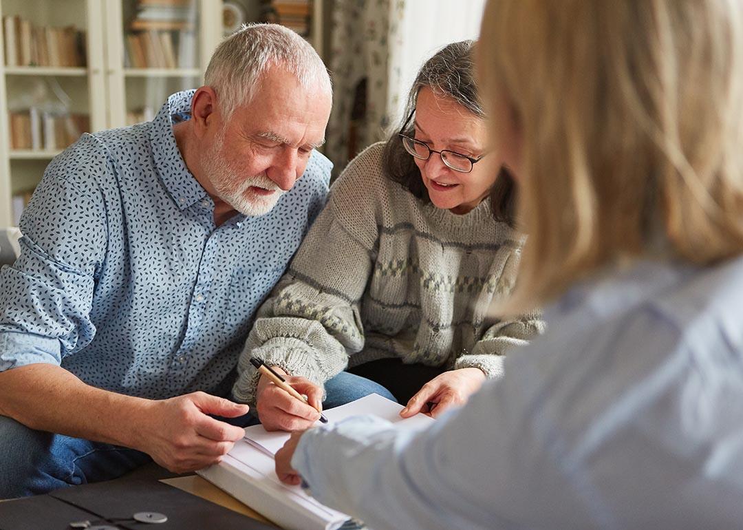 An elderly couple signing documents with a legal professional.