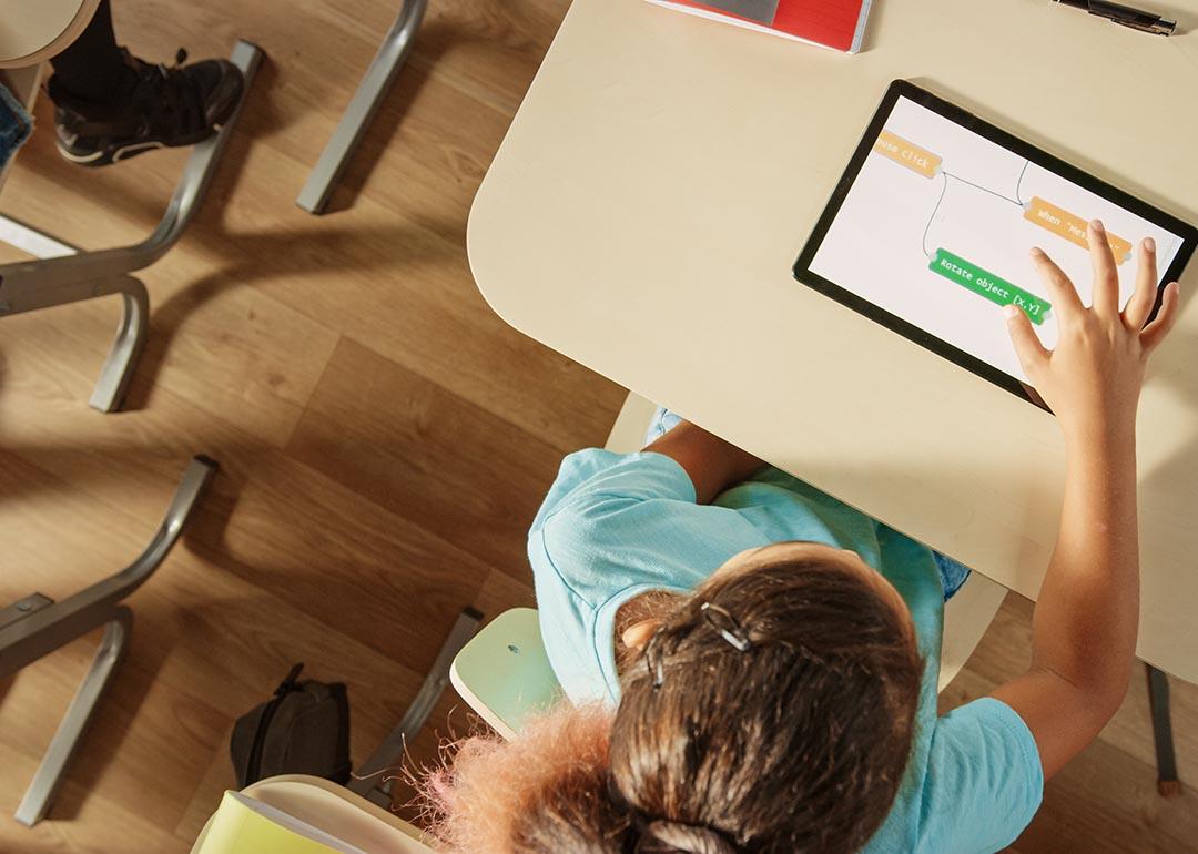 High-angle view of tween student using a tablet on a desk in the classroom. 