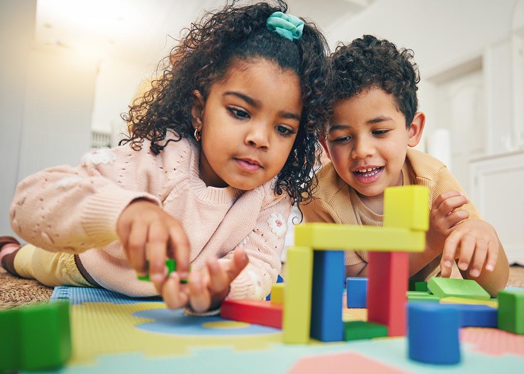 Two children and laying on their stomachs on the floor with toys for playing with building blocks.