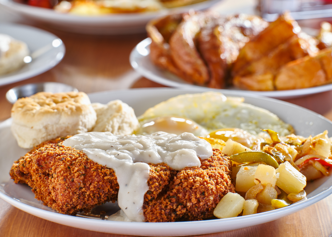 Chicken fried steak covered in gravy with sunny side up eggs, biscuits and potatoes on a plate