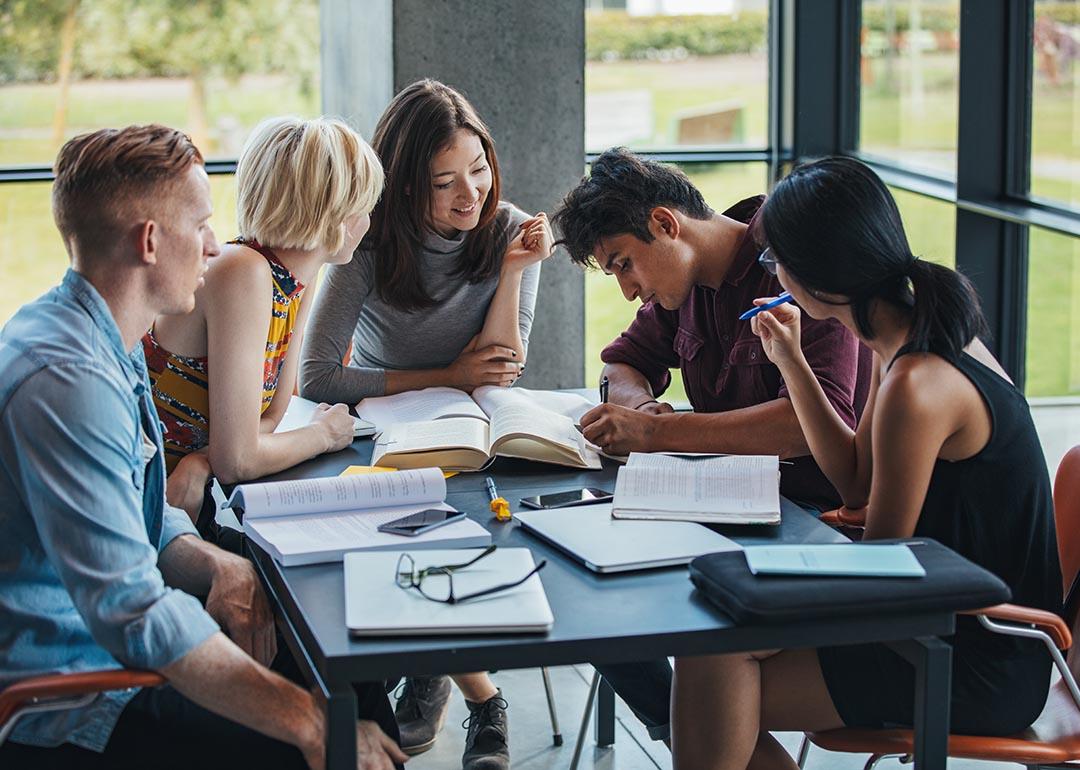 A group of five young adult students engaged in a discussion around a table.