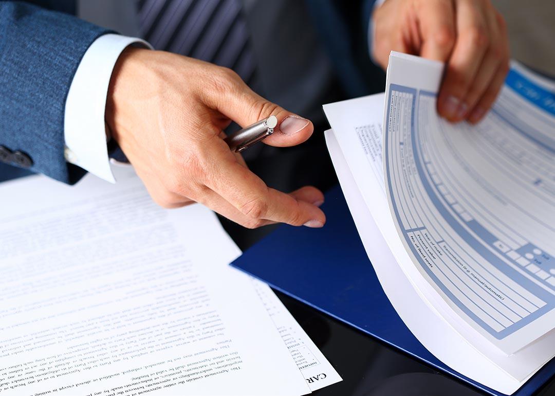 Close up of hands of person wearing a suit shuffling insurance forms and holding a pen.