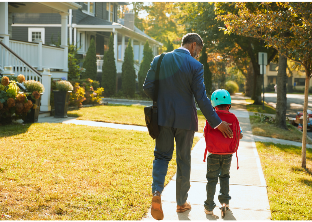 Parent walking with child on the sidewalk in the suburbs.