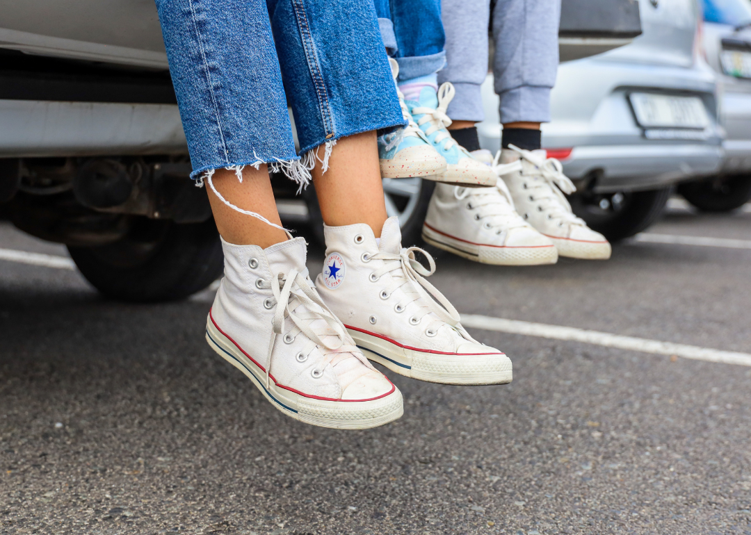 Cropped legs of an adult, teenager and toddler sitting together on the back of a car wearing sneakers