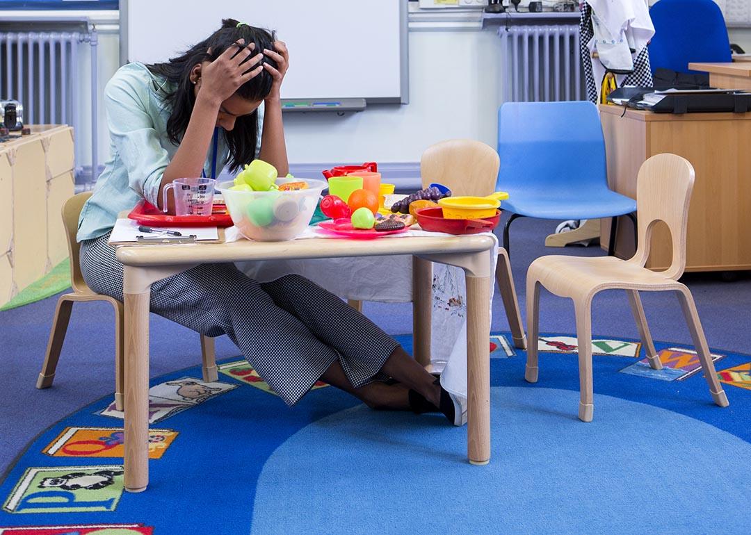 Teachers sitting in a young student classroom with head in her hands.