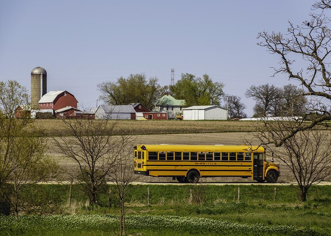 KINGSTON, ILLINOIS A public school bus passes by a large farmstead along a rural road on a spring day, with the edge of a county forest preserve in the foreground.