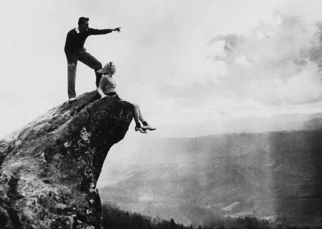 Perched atop Blowing Rock, an unidentified couple as they look out over Great Smoky Mountains National Park, North Carolina, circa 1930.