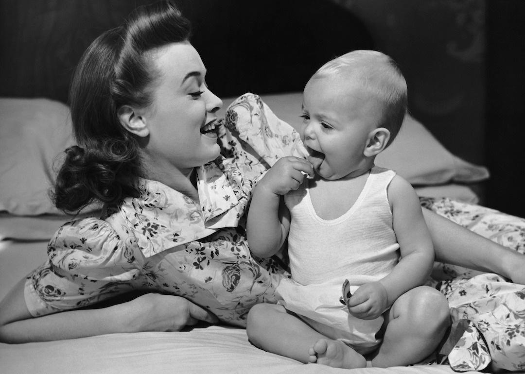 Mother watching her baby eat a cookie, circa 1950s.